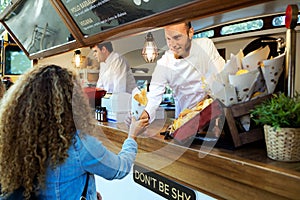 Beautiful young woman buying barbecue potatoes on a food truck.