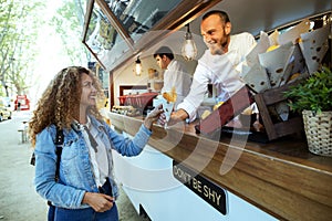 Beautiful young woman buying barbecue potatoes on a food truck.