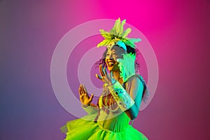 Beautiful young woman in carnival and masquerade costume on gradient studio background in neon light