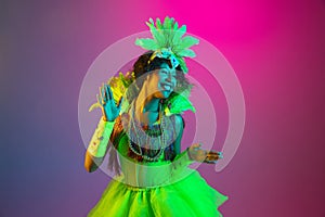 Beautiful young woman in carnival and masquerade costume on gradient studio background in neon light