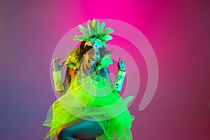 Beautiful young woman in carnival and masquerade costume on gradient studio background in neon light