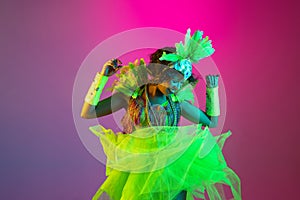 Beautiful young woman in carnival and masquerade costume on gradient studio background in neon light