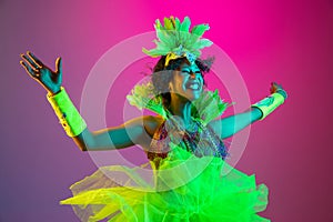 Beautiful young woman in carnival and masquerade costume on gradient studio background in neon light