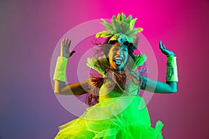 Beautiful young woman in carnival and masquerade costume on gradient studio background in neon light