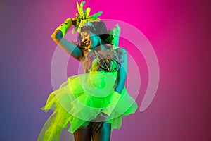 Beautiful young woman in carnival and masquerade costume on gradient studio background in neon light