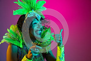 Beautiful young woman in carnival and masquerade costume on gradient studio background in neon light