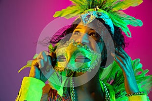 Beautiful young woman in carnival and masquerade costume on gradient studio background in neon light