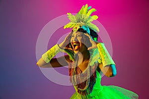 Beautiful young woman in carnival and masquerade costume on gradient studio background in neon light