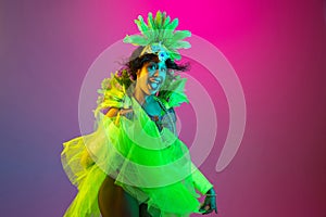 Beautiful young woman in carnival and masquerade costume on gradient studio background in neon light