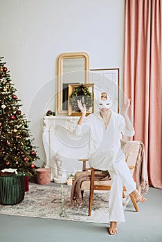 Beautiful young woman in a carnival rabbit mask and white costume celebrates the new year near the Christmas tree in a modern