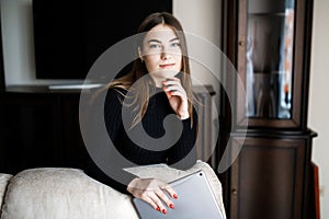 Beautiful young woman in casual clothes is using a digital tablet and smiling while sitting on couch at home