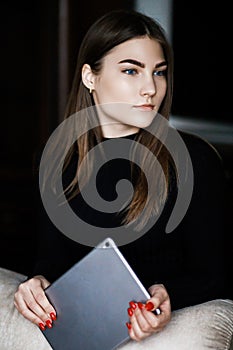 Beautiful young woman in casual clothes is using a digital tablet and smiling while sitting on couch at home