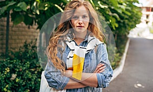 A beautiful young woman in a casual outfit posing outdoors. Pretty female student with long red curly hair standing in the city