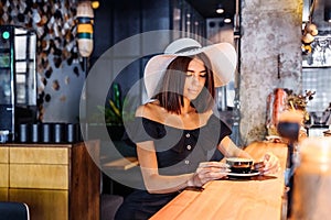 Beautiful, young woman of Caucasian nationality sitting at the bar and enjoying delicious morning coffee, cappuccino or americano