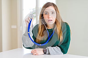 Beautiful young woman checking health with stethoscope scared in shock with a surprise face, afraid and excited with fear