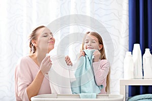 Beautiful young woman and child girl having fun while doing laundry at home