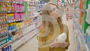 Beautiful young woman is choosing household products while doing shopping at the supermarket