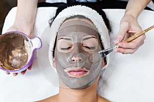 Beautiful young woman with clay facial mask in beauty spa. Detox