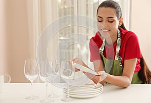 Beautiful young woman with clean dishes in kitchen