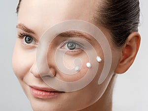 Beautiful Young Woman with Clean Fresh Skin. Drops of cream are applied on the cheek. Hand near the face. Girl beauty face care.