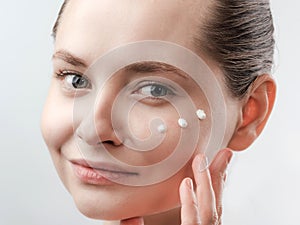 Beautiful Young Woman with Clean Fresh Skin. Drops of cream are applied on the cheek. Hand near the face. Girl beauty face care.