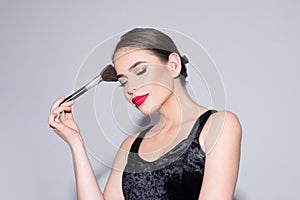 Beautiful young woman with clean fresh skin putting blush with cosmetic brush.
