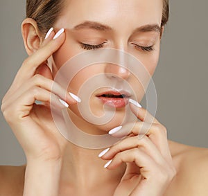 Beautiful young woman with clean fresh skin touching her face over grey background.