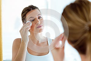 Beautiful young woman is cleaning her face while looking in the bathroom.