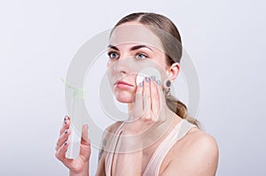 Beautiful young woman cleansing her face with cotton sponge