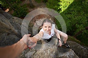 Beautiful young woman climbing on rock outdoors in summer. Top view. Happy girl climbing rock trekking outdoors