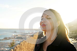 Beautiful young woman with closed eyes breathing with wind on her face relaxing enjoying sun at sunset. Beauty sunshine girl side