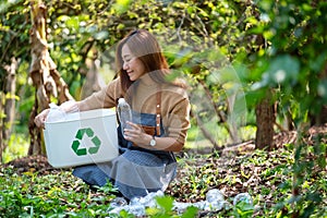 A beautiful young woman collecting and putting plastic bottles into a recycle bin in the outdoors