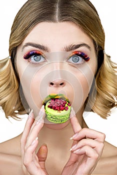 Beautiful young woman with colored rainbow eyelashes and bright makeup eats macaroon sweetie, close-up
