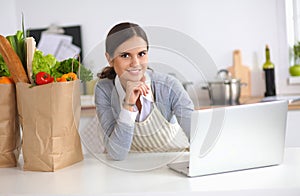 Beautiful young woman cooking looking at laptop