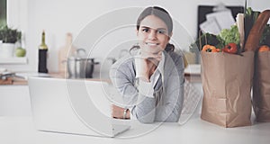 Beautiful young woman cooking looking at laptop screen with receipt in the kitchen