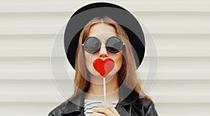 beautiful young woman covering her mouth with red heart shaped lollipop on a white background