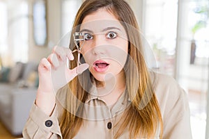 Beautiful young woman curling eyelashes using eyelash curler scared in shock with a surprise face, afraid and excited with fear