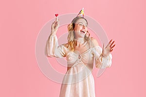 Beautiful young woman in cute dress, laughing, celebrating birthday against pink studio background. Happy