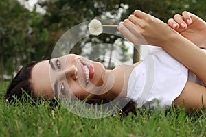 Beautiful young woman with dandelion lying on green grass in park. Allergy free concept