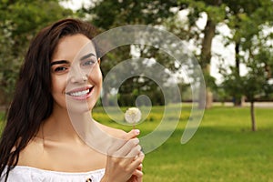 Beautiful young woman with dandelion in park, space for text. Allergy free concept