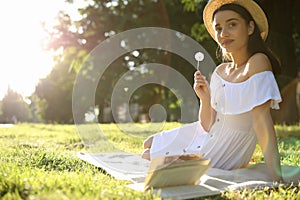 Beautiful young woman with dandelion in park on sunny day. Space for text