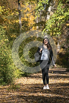 Beautiful young woman with dark hair walks along the alley of autumn park and enjoys a warm day. Lonely girl in forest