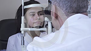 Beautiful young woman do eye test at clinic sitting in front of doctor in white medical coat looking in eye test machine