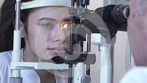 Beautiful young woman do eye test at clinic sitting in front of doctor in white medical coat looking in eye test machine