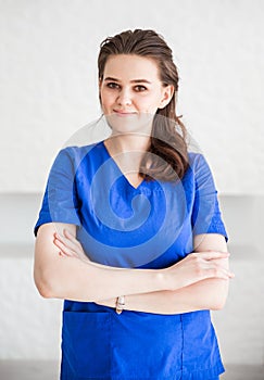 Beautiful young woman doctor posing in blue medical suit against white wall background