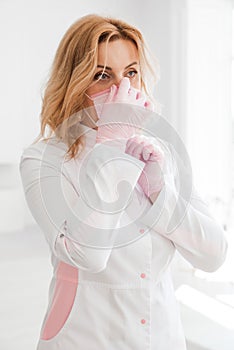 Beautiful young woman doctor in a white medical gown puts on a protective mask on her face