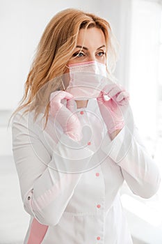 Beautiful young woman doctor in a white medical gown puts on a protective mask on her face