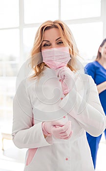 Beautiful young woman doctor in white uniform puts on a protective mask on her face