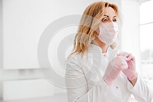 Beautiful young woman doctor in white uniform puts on a protective mask on her face