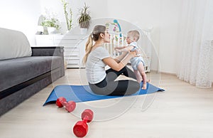 Beautiful young woman doing fitness exercises with her baby boy on floor at home